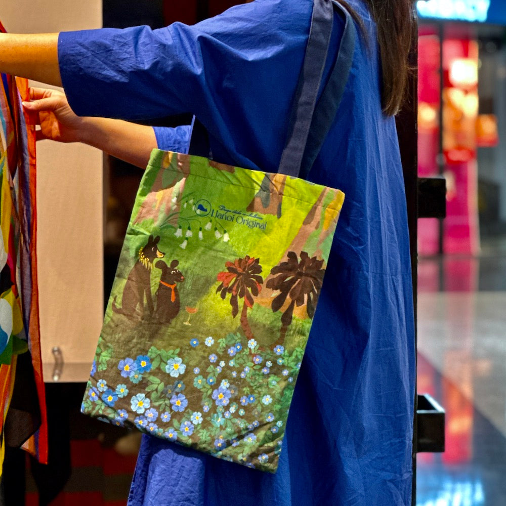 Image show a girl wearing the Tote bag by Hanoi Original, depicts friendship of a dog, and a mouse among gumtree forest and blue meadow  flowers